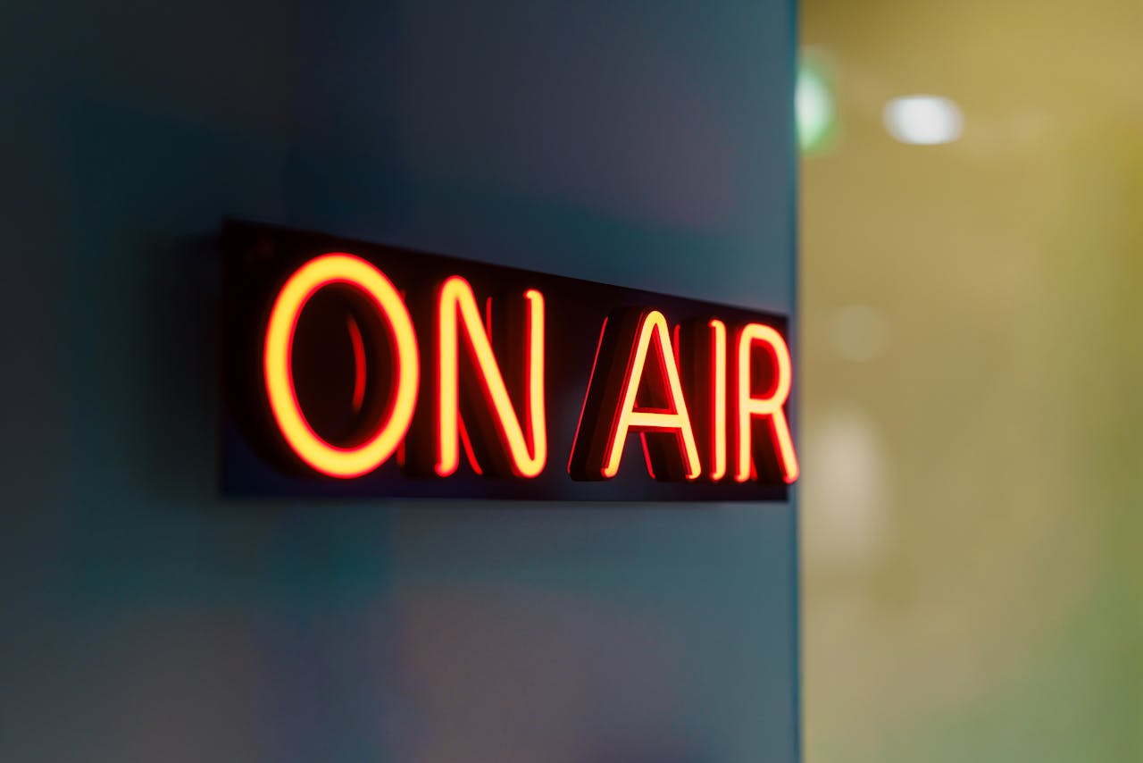 Close-up of a glowing On Air neon sign in a dimly lit studio setting, symbolizing live broadcasting.